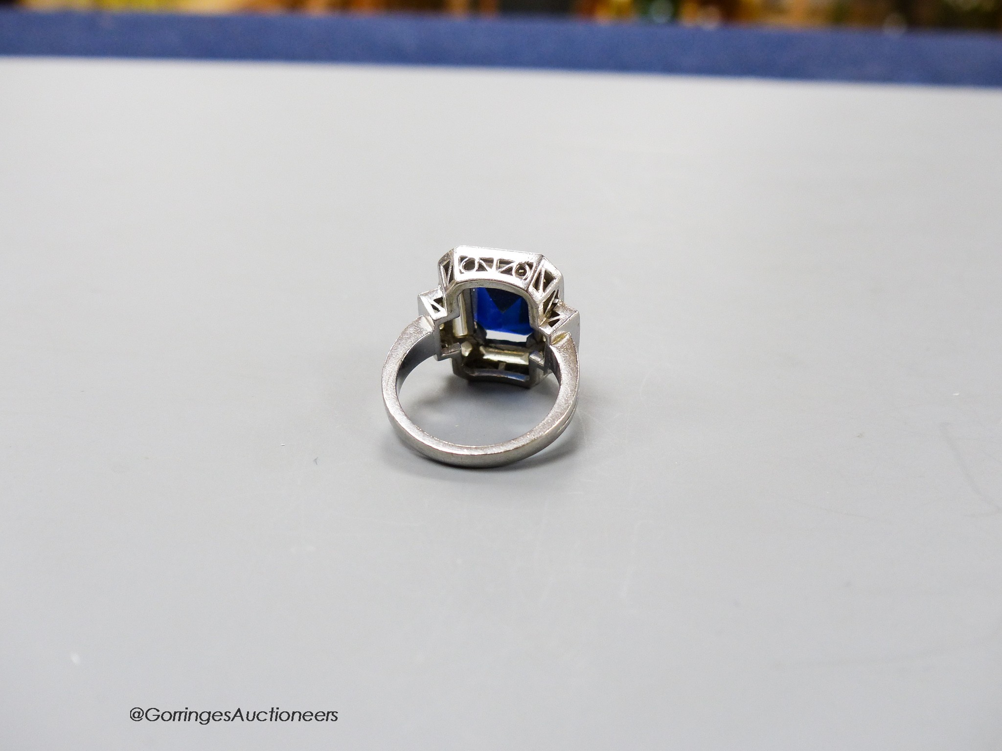 A white metal (stamped plat? synthetic sapphire, baguette and trapeze cut diamond set dress ring, size L, gross weight 11.1 grams